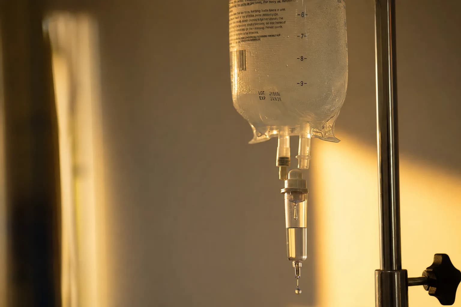 A clear medical IV bag on a stand with warm sunlight filtering through - precision radiation, delivered drop by drop